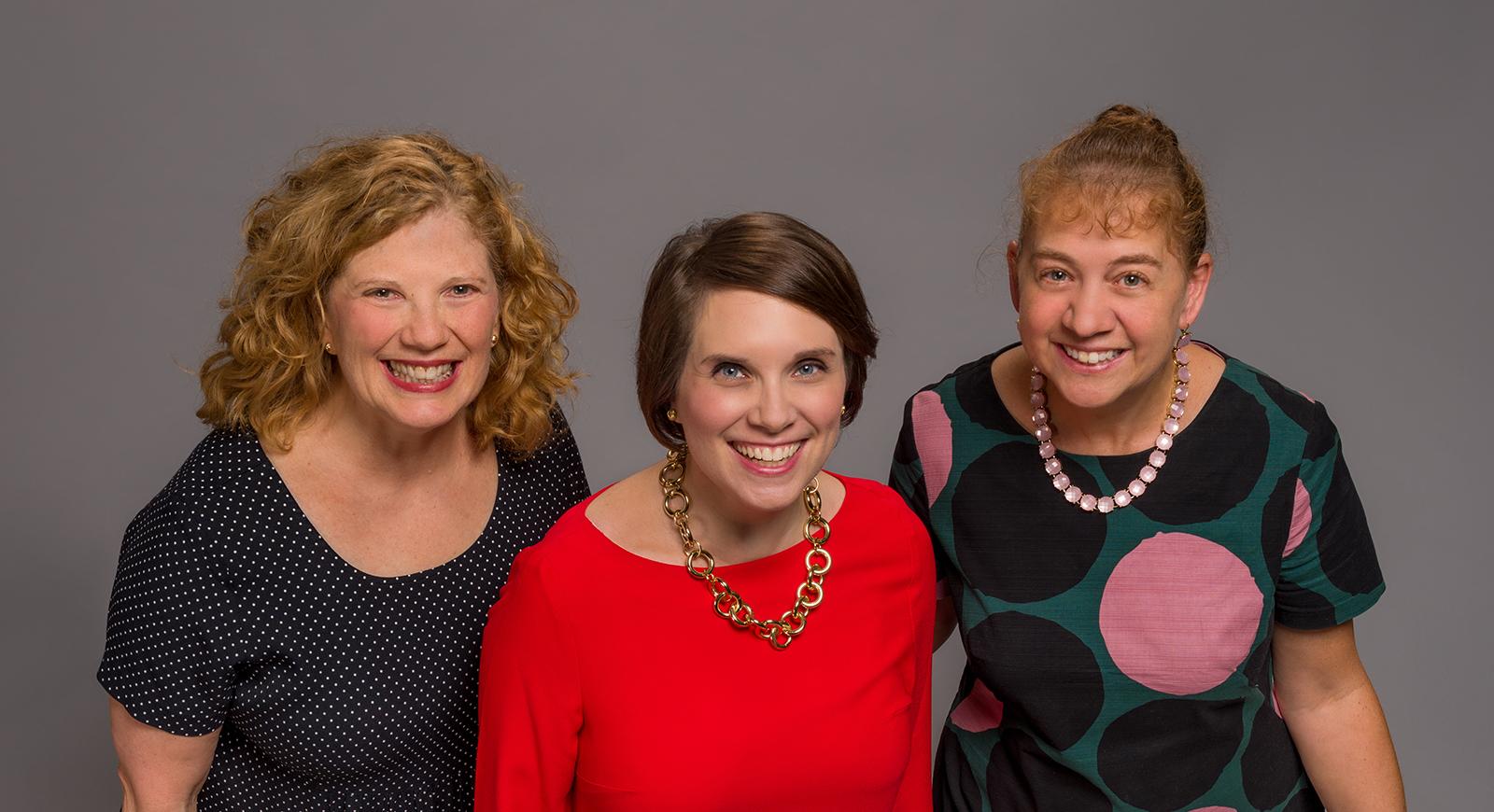 Photo of three women in professional clothing, smiling for the camera